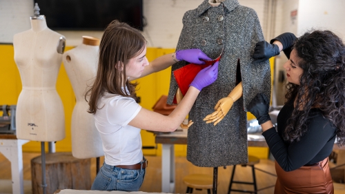 two costume studies students arrange a grey 50s style suit on a mannequin