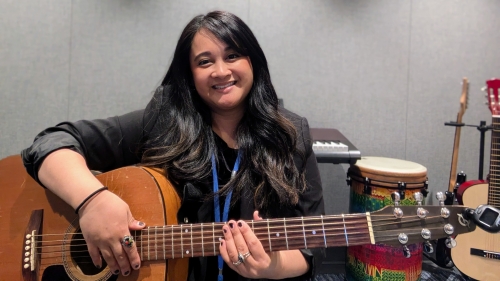 Music Therapy alumna Leilani Victor holding guitar and smiling at camera