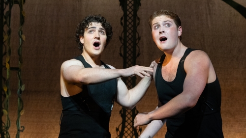 Two male actors on stage in black tank top and leggings looking scared while singing