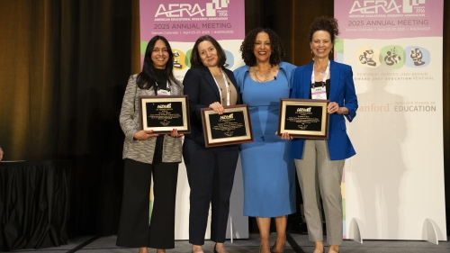 Four women stand on a stage in front of AERA banners. Three hold plaques.