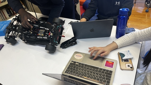People sit around a table with laptops and robotics equipment