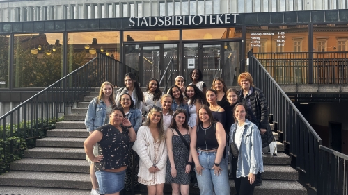 A group of students poses in front of a Swedish library building.