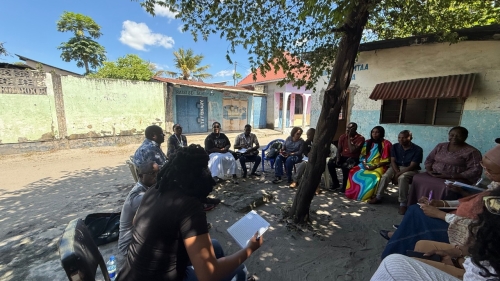 Outdoors, a group of people sits in a circle in conversation