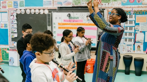 A teacher directs students playing musical instruments in a classroom