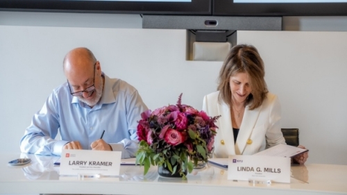 Kramer and Mills sign documents at a table.