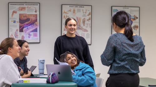 A group of students talking and laughing around a table with a laptop and papers.