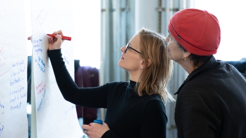 A woman writes on a poster while another watches