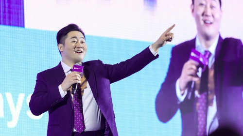 Dongyang Fei on stage with microphone and large image of himself behind him