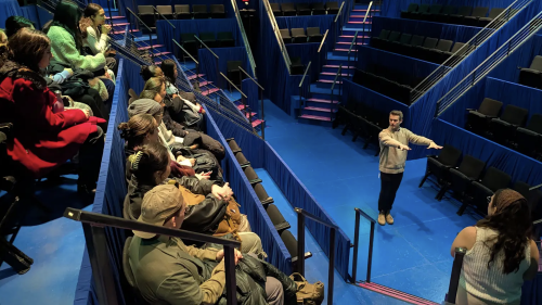 Students looking down the stage from the seating area as they listen to their host.