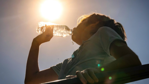 A person drinks water under the sun