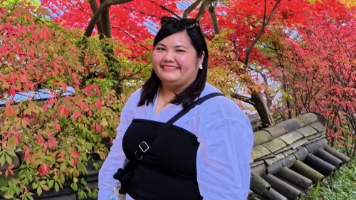 Smiling headshot of Patricia Librea in front of a background of trees with green and red leaves
