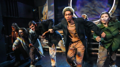 Group of actors hunched over walking toward camera on stage