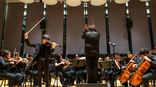 Solo violinist striking a huge stroke on the instrument while conductor leads the concert