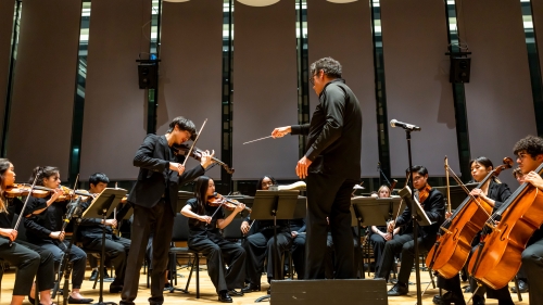 Symphony performing while conductor points to soloist violin player