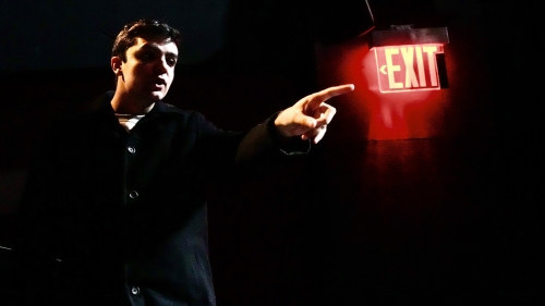 Student on dark stage pointing at lit up exit sign