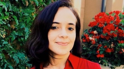 A picture of woman outside in a red blouse with dark hair smiling at the camera.