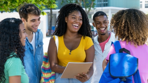 image captures 5 high school students gathered togeter. The students sit in a circle as they wor together. The photo is centerd around an African American female with shoulder lnegth hair, wearing a yellow top.