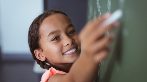 Young girl writing on chalk board.