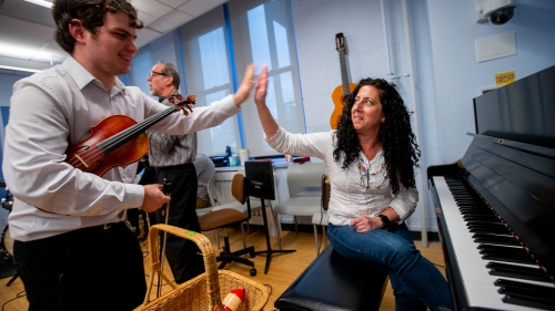 On student at piano and another holding violin giving each other a high five
