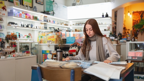 Student working in a shop as an intern. Lots of bright accessories on white shelves.
