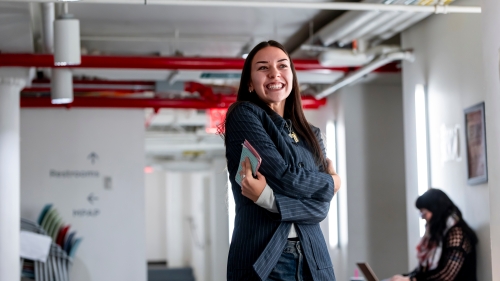 Student posing giving herself a hug in a basement cellar with white walls and red painted pipes