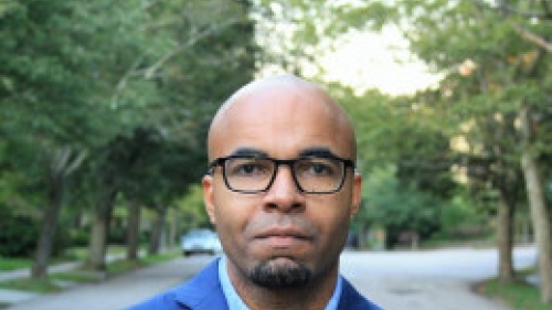 Headshot of Mario Small standing outdoors with arms crossed, wearing glasses and a blue blazer over a light shirt, looking at the camera on a tree-lined path.