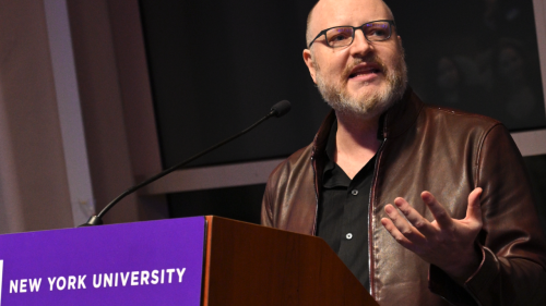 Sam Howard-Spink speaks at a podium with "New York University" on it