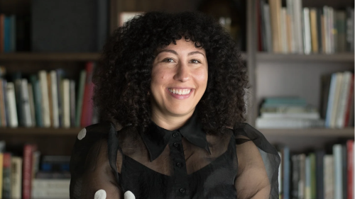 Christina is smiling in the center of the frame and has her arms crossed.