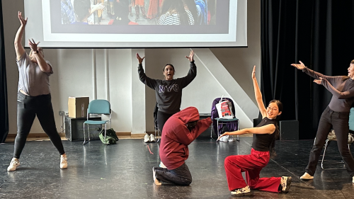 Theatre students doing movements in a large studio with a photo screen behind them