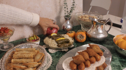 A hand adjusts a pomegranate in a spread of food on a dining table,
