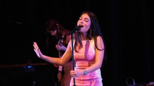 Student singing at mic on stage wearing a pink dress