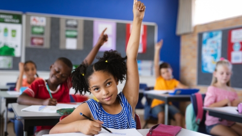 A young girl in classroom raising her hand