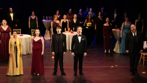 A row of opera singers with singers behind them readying to take a bow