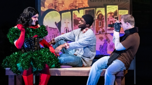 Three cast members from RENT acting on stage. One character filming the other two singing to each other.