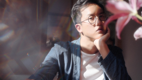 Student posing with lens blurred and a pink flower in front of him