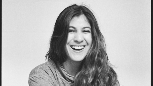 Black and white photo, Juliana is wearing a long sleeve shirt and is sitting center of frame smiling widely.