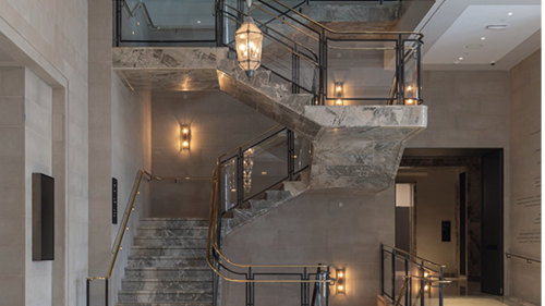 A stairway made of gray and white granite, thin gold hardware, and glass panels.