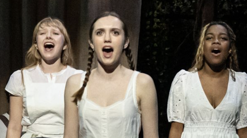 Close up of three students in white dresses singing on stage