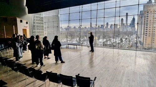 Students looking at the speaker in front of huge windows in Lincoln Center Apple Room.