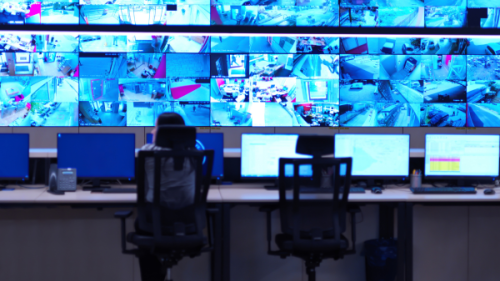 Person sitting at a desk looking at surveillance footage on various tv screens