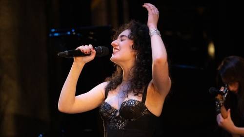 Singer performing with arm over her head and eyes closed.