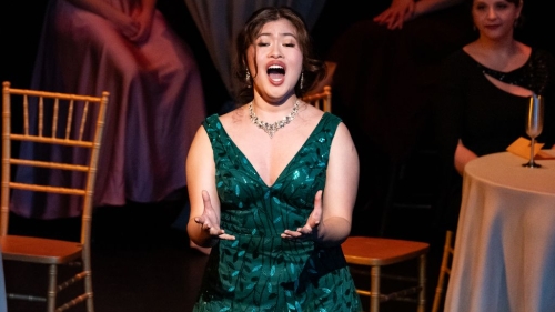 Student in V neck green sparkly dress singing opera on stage