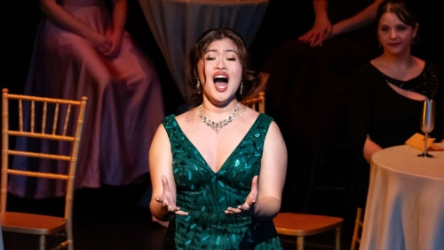 Student in V neck green sparkly dress singing opera on stage