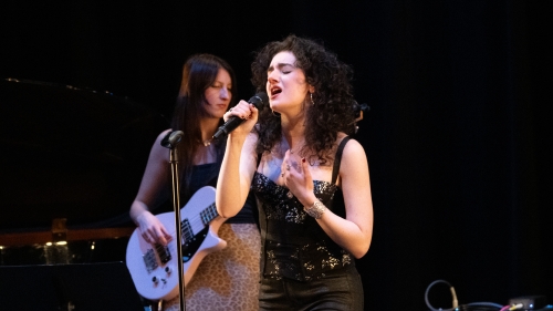 Student on stage singing into microphone with a guitarist backup