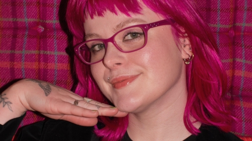 Student with raspberry colored hair posting in front of raspberry checked backdrop