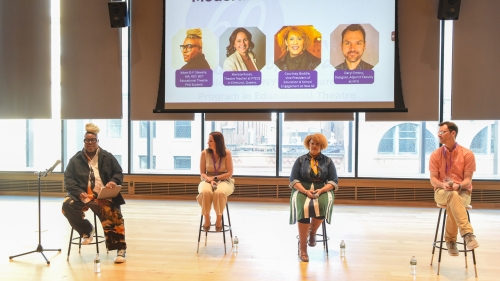 1 moderator and 3 panelists sitting on stools in front of a projected slide with their names, headshots, and titles