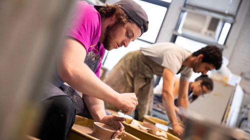 A student shapes a pot at the wheel.
