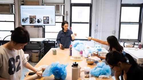 Fan Qi examines a student's work at a table.
