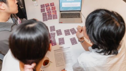 Students sit at a desk with cards and a laptop.
