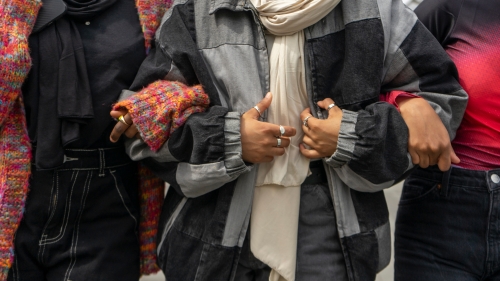 Three young women stand with arms linked, their heads not visible